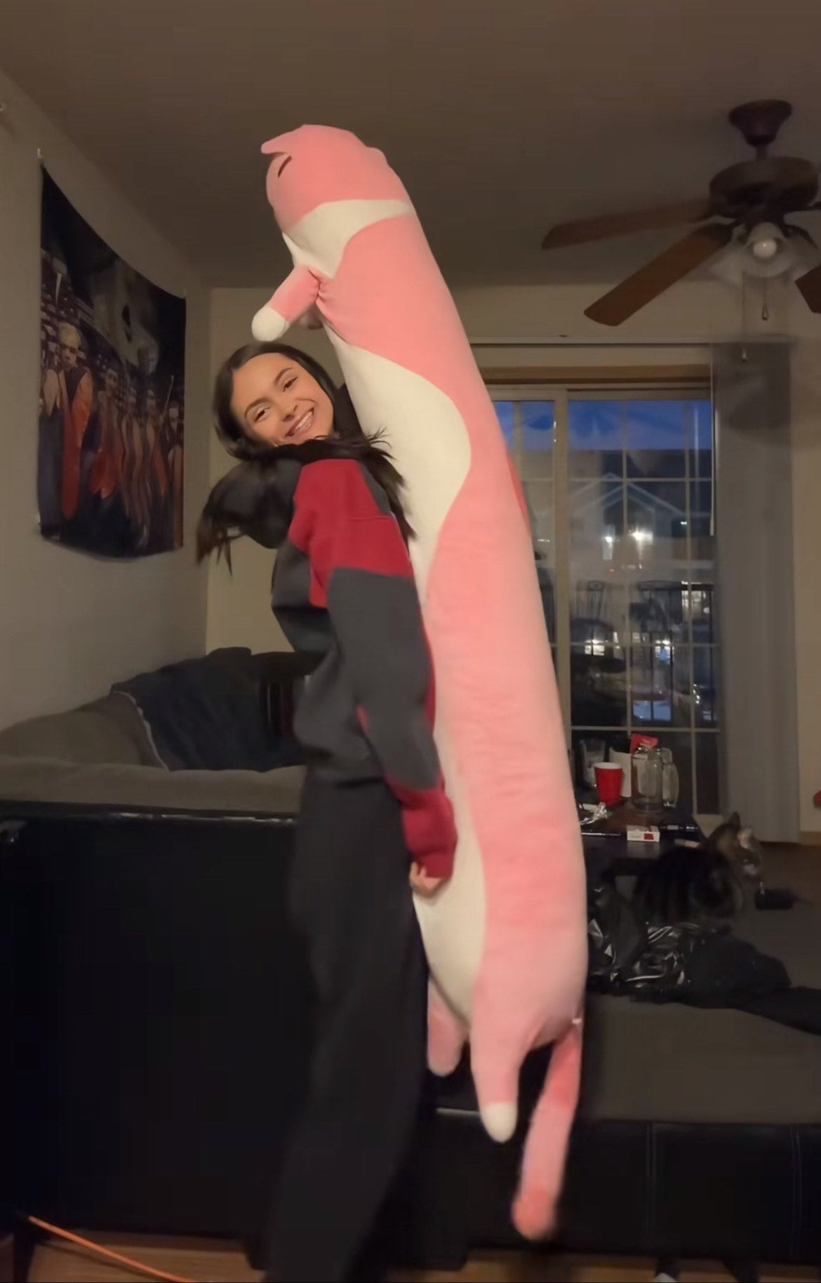 Person holding a large pink and white plush toy in a living room.